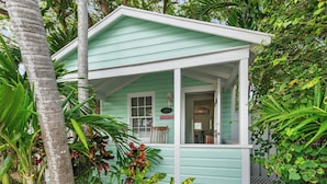 A small, single-story building with a porch, surrounded by lush greenery. - ~ROYAL POINCIANA COTTAGE~ Come and indulge yourself in some KW sunshine! (Key West)