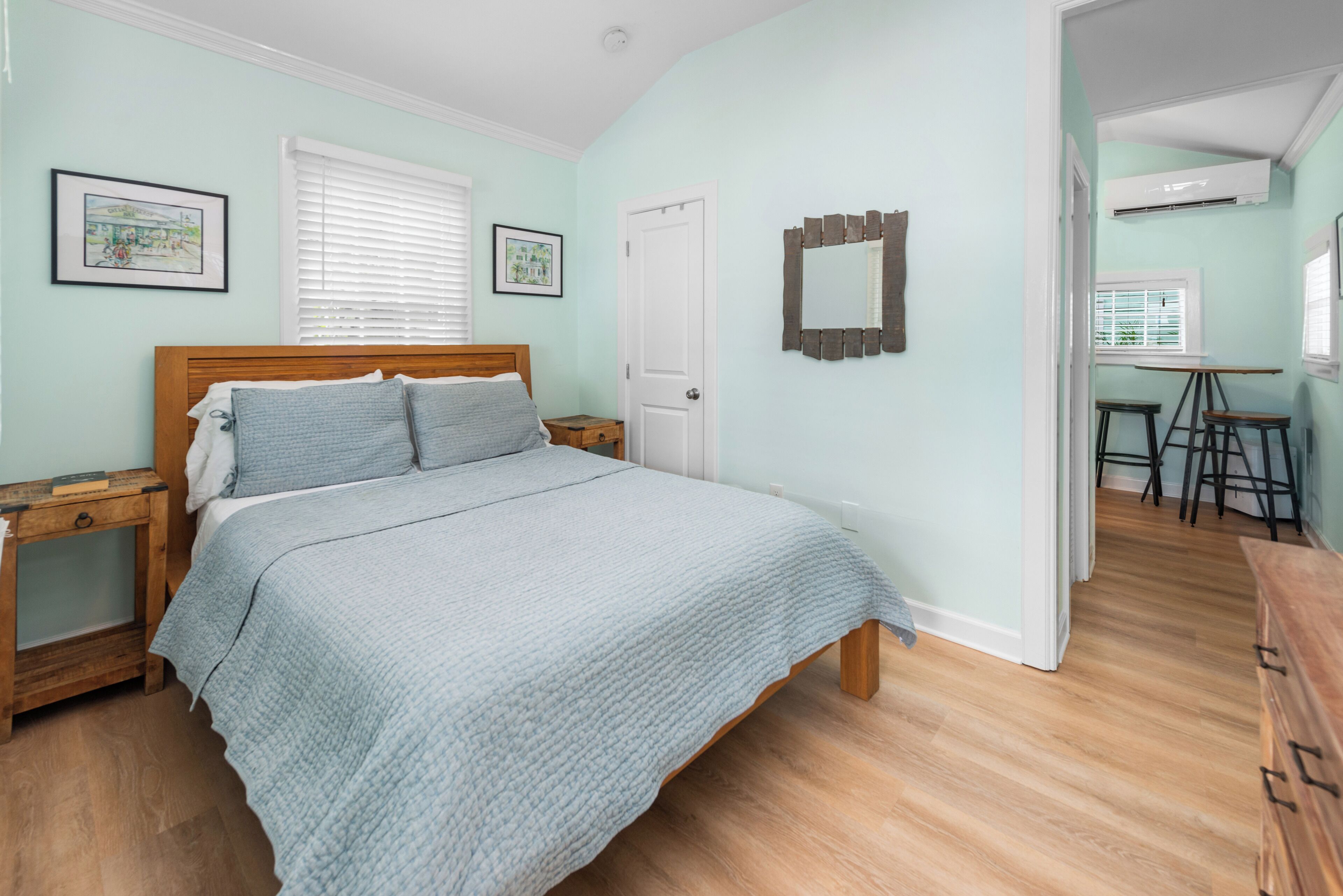 A bedroom with a bed, wooden nightstands, a door, and a small desk with chairs.