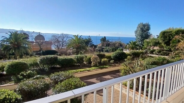 Un balcón con vistas a un jardín ajardinado, un cuerpo de agua y un edificio distante con una cúpula.