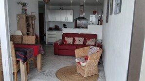 Una sala de estar con un sofá rojo, sillas de mimbre, una mesa de centro y una cocina al fondo.