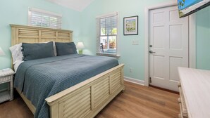A bedroom with a bed, nightstands, a door, and windows. - ~MARGARITA COTTAGE~ Bask in sunshine and lounge by your pool in paradise. (Key West)