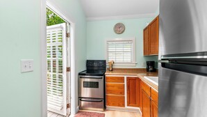 A kitchen with a stainless steel refrigerator, a built-in oven, wooden cabinets, a window with blinds, and a door leading to an outdoor area. - ~MARGARITA COTTAGE~ Bask in sunshine and lounge by your pool in paradise. (Key West)
