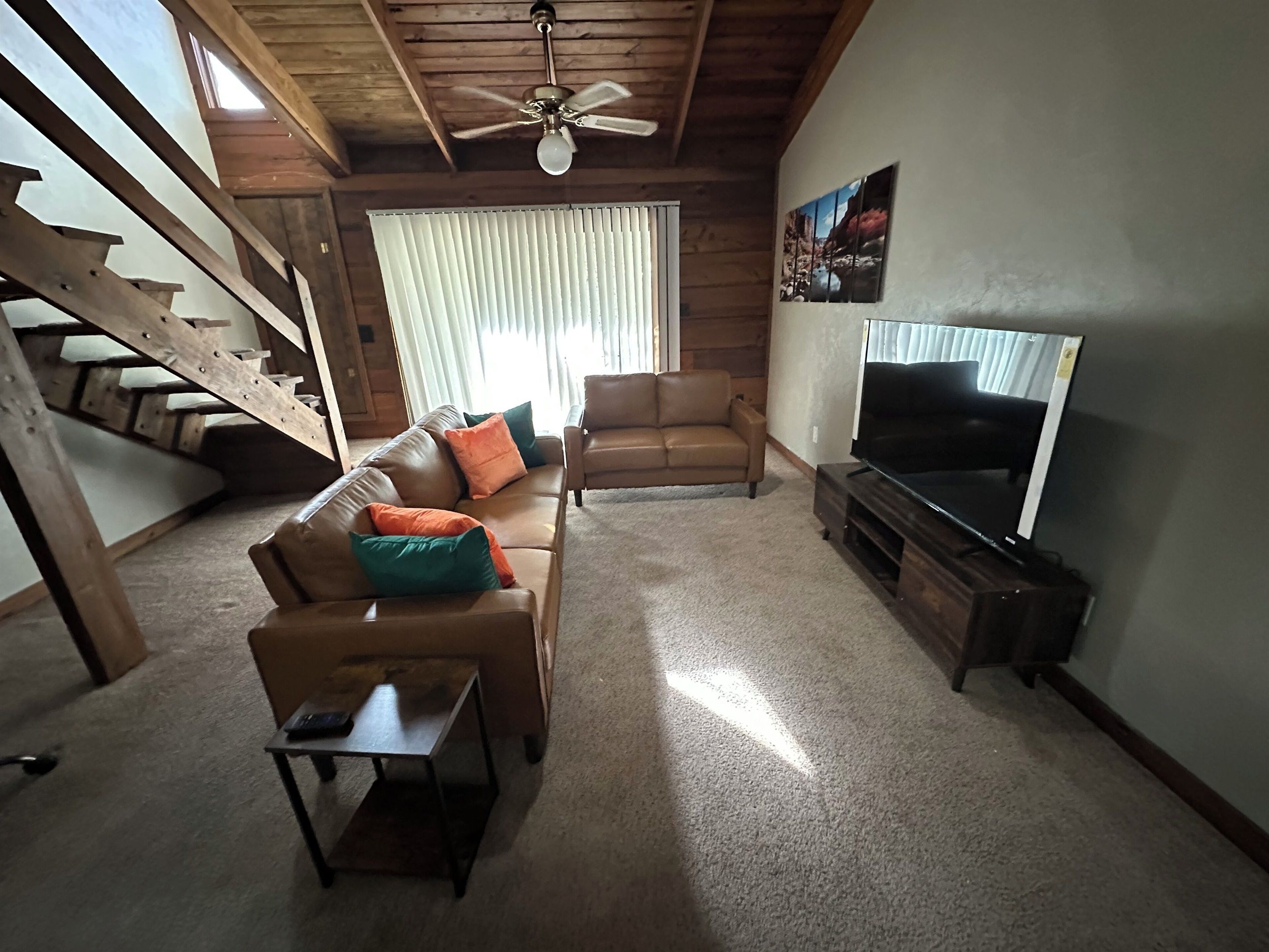 A living room with a wooden staircase, a brown leather sofa, a television, and a ceiling fan.