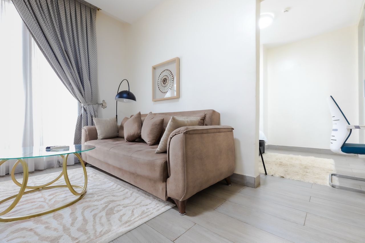 A living room with a beige sofa, a glass coffee table, a framed artwork, and a modern lamp.