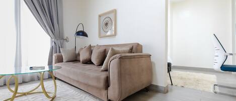 A living room with a beige sofa, a glass coffee table, a framed artwork, and a modern lamp.