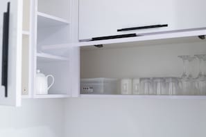 A white cabinet with a handle, containing a white teapot, a transparent container, and several clear glassware items. - Turquaz Resisdence (Accra)
