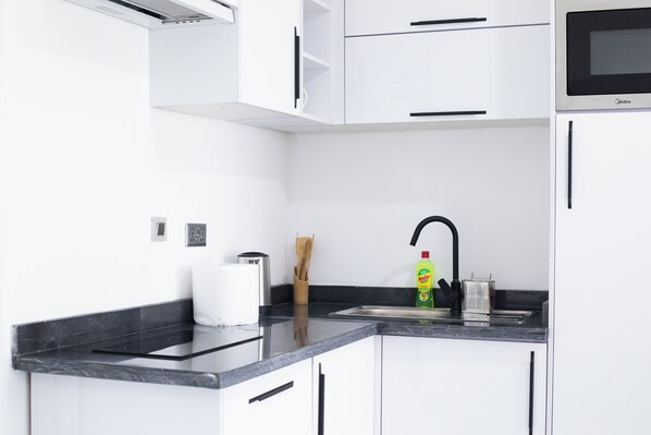 Una cocina moderna con armarios blancos, encimera negra, pileta de acero inoxidable y un microondas.