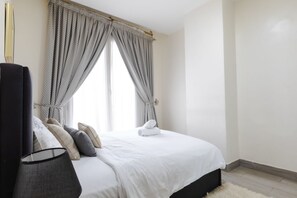 Un lit bien fait, avec du linge de lit blanc, une tête de lit noire et un rideau à motifs gris.