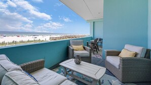 A balcony with wicker furniture, a view of the beach, and a clear sky.