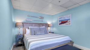 A bedroom with a bed, two bedside tables, a bench, a wall-mounted paddle, and a framed picture.