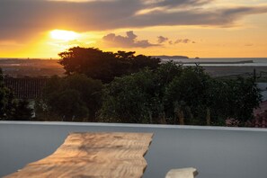 A sunset view from a balcony with a wooden floor, trees, and a distant shoreline. - Le Moulin Indigo, Peniche (Atouguia da Baleia)