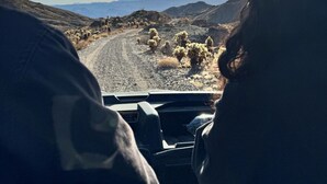 A vehicle's interior with a dashboard displaying a sunroof and a view of a desert landscape with mountains in the distance.