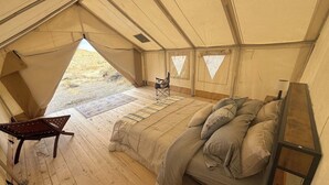 A tented room with a bed, a chair, and a small table.