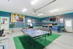 A room with a ping pong table, a foosball table, and a TV mounted on the wall.