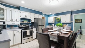 A modern kitchen with white cabinets, stainless steel appliances, and a dining area with a table set for four. - The Bourbon Trail Bungalow Ping Pong/Foosball/Bar/Firepit (Mount Washington)