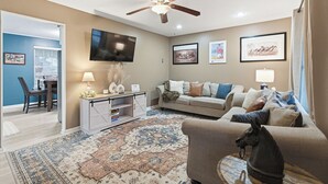 A living room with a ceiling fan, a flat-screen TV, a sofa, a coffee table, and a rug. - The Bourbon Trail Bungalow Ping Pong/Foosball/Bar/Firepit (Mount Washington)