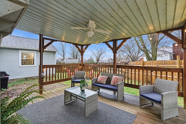 A covered deck with wicker furniture, a ceiling fan, and a view of the backyard.