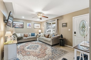 A living room with two sofas, a coffee table, a rug, a ceiling fan, and framed pictures on the walls.