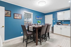 A dining area with a blue wall, a white door, and a kitchen with white cabinets.