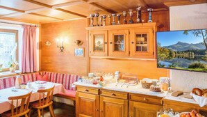 A cozy breakfast setup with wooden cabinets, a dining table, and a scenic view on the wall. - Pension Rainhof (Kitzbuhel)