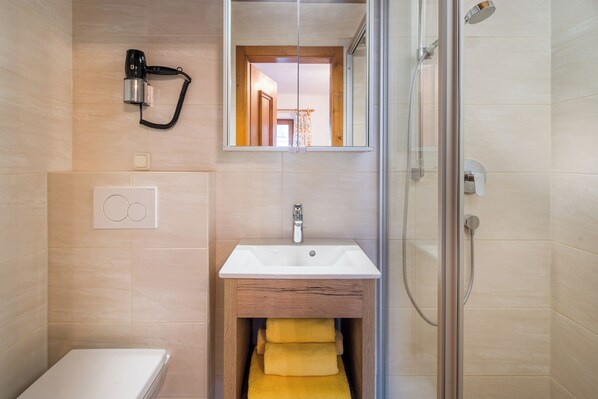 A modern bathroom with a shower, a sink, and a hairdryer mounted on the wall. - Pension Rainhof (Kitzbuhel)