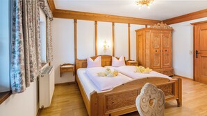 A wooden-framed bed with floral curtains, a nightstand, and a wooden wardrobe in a room with wooden flooring and a chandelier. - Pension Rainhof (Kitzbuhel)