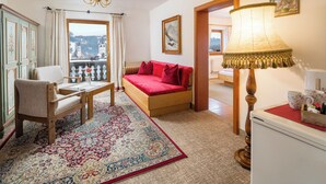A cozy room with a bed, a chair, a table, a lamp, and a view of a mountain through a window. - Pension Rainhof (Kitzbuhel)