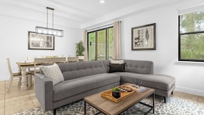 A modern living room with a grey sectional sofa, a wooden coffee table, and a dining area with a white table and chairs. - Dluxx Tranquil 4BR Cozy Home w Full Kitchen 8115 (Davenport)