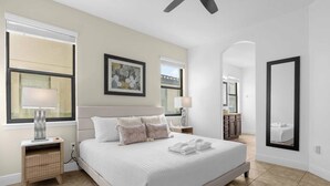 A bedroom with a large bed, bedside lamps, a nightstand, a mirror, and a window with blinds. - Dluxx Tranquil 4BR Cozy Home w Full Kitchen 8115 (Davenport)