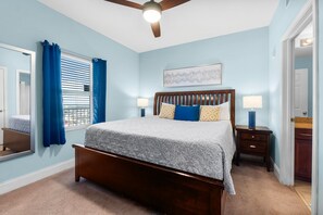 A bedroom with a wooden bed, a ceiling fan, and a window with blue curtains.