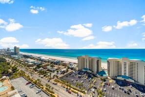 A coastal hotel with multiple high-rise buildings, a parking lot, and a beach in the background.