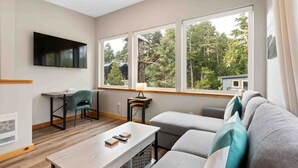 A modern living room with a TV, a sofa, a table, and a window with a view of trees.