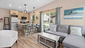 A modern kitchen with wooden cabinets, a refrigerator, and a dining area with bar stools. - SS#8-Kitesurfer-Spring Cove, Terrace Beach, Sauna! (Ucluelet)