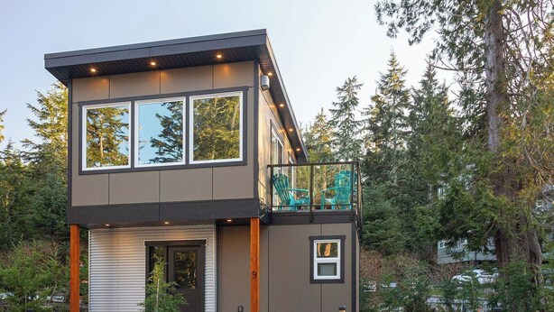 Une maison moderne à deux étages, dotée d’un balcon, de grandes fenêtres et d’une allée gravillonnée.