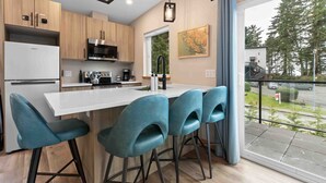 Une cuisine moderne avec des meubles en bois, un îlot central blanc doté de tabourets de bar et une grande fenêtre offrant une vue sur l’extérieur.