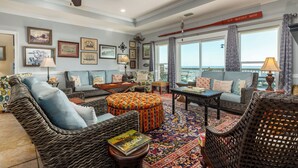 A spacious living room with wicker furniture, a large window offering a view of the sea, and a ceiling fan. - "Wahoo" Gulf Beachfront, 4 Bedroom/4 Bath, Sleeps 14, Pet Friendly, Cargo Lift (Dauphin Island)