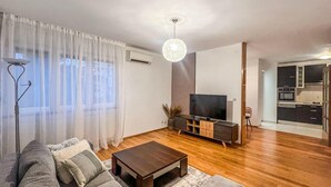 A modern living room with a sofa, coffee table, TV, and kitchen in the background.