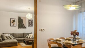 A modern living room with a gray sofa, a dining table set for four, and a vase with flowers on the table.