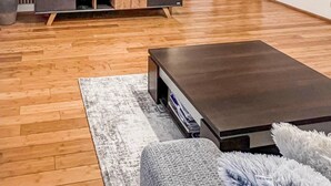 A modern living room with a flat-screen TV, wooden flooring, a dark coffee table, and a fluffy white sofa.