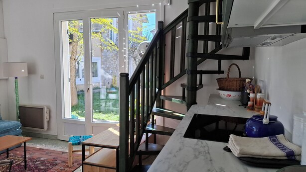 Eine moderne Küche mit Marmorarbeitsplatte, einer schwarzen Treppe und Blick auf einen Garten durch Glastüren.