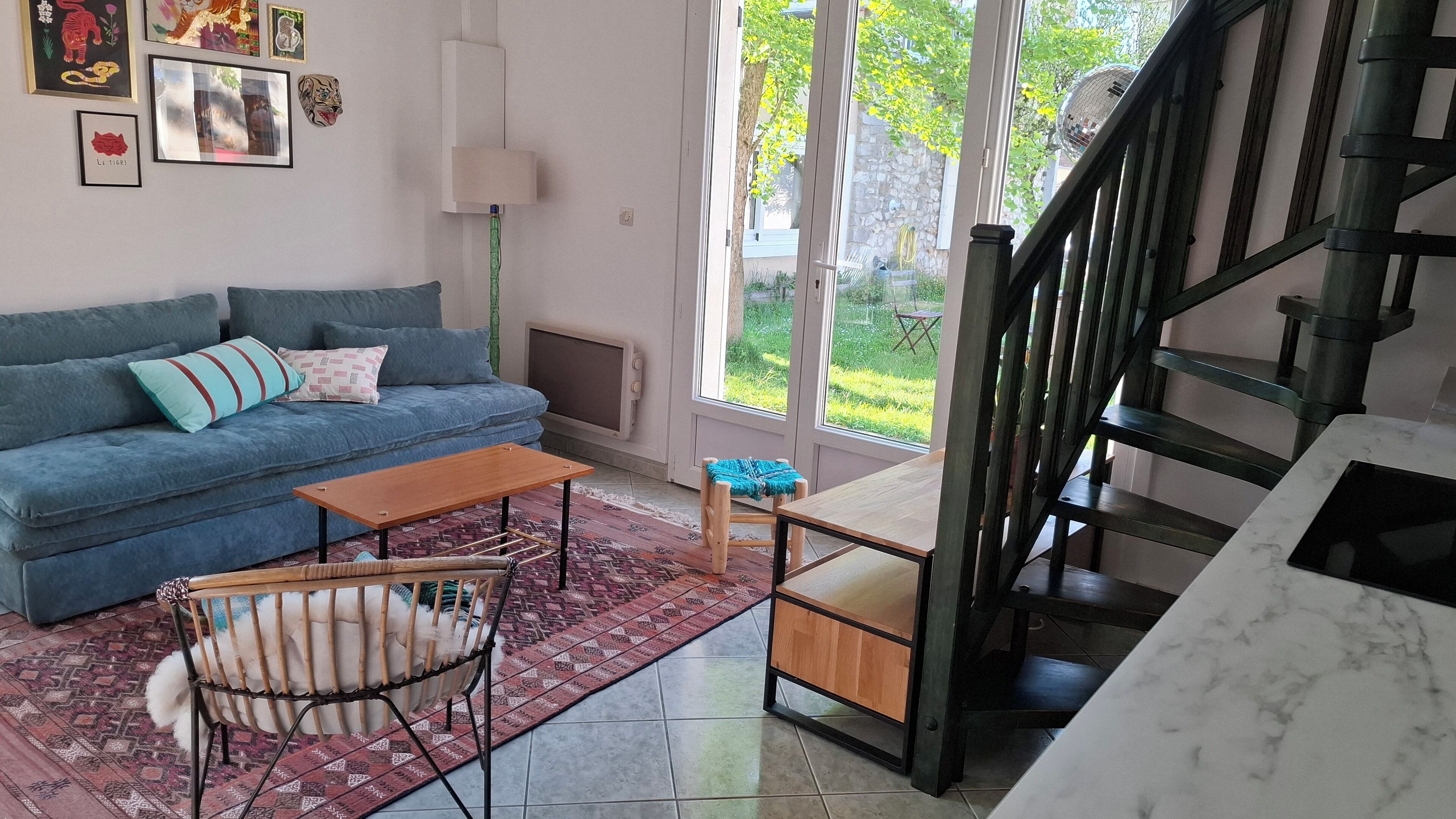 Ein Wohnzimmer mit einem blauen Sofa, einem Holztisch, einem gemusterten Teppich, einem kleinen Hocker und einer Treppe.