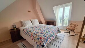 Ein Schlafzimmer mit Bett, Nachttisch, Kommode, Schaukelstuhl und einem Fenster mit Vorhängen.