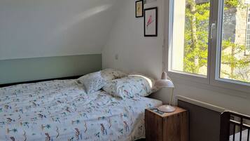 Ein Schlafzimmer mit Bett, Nachttisch, Sessel und einem Fenster mit Blick auf Bäume und Gebäude.