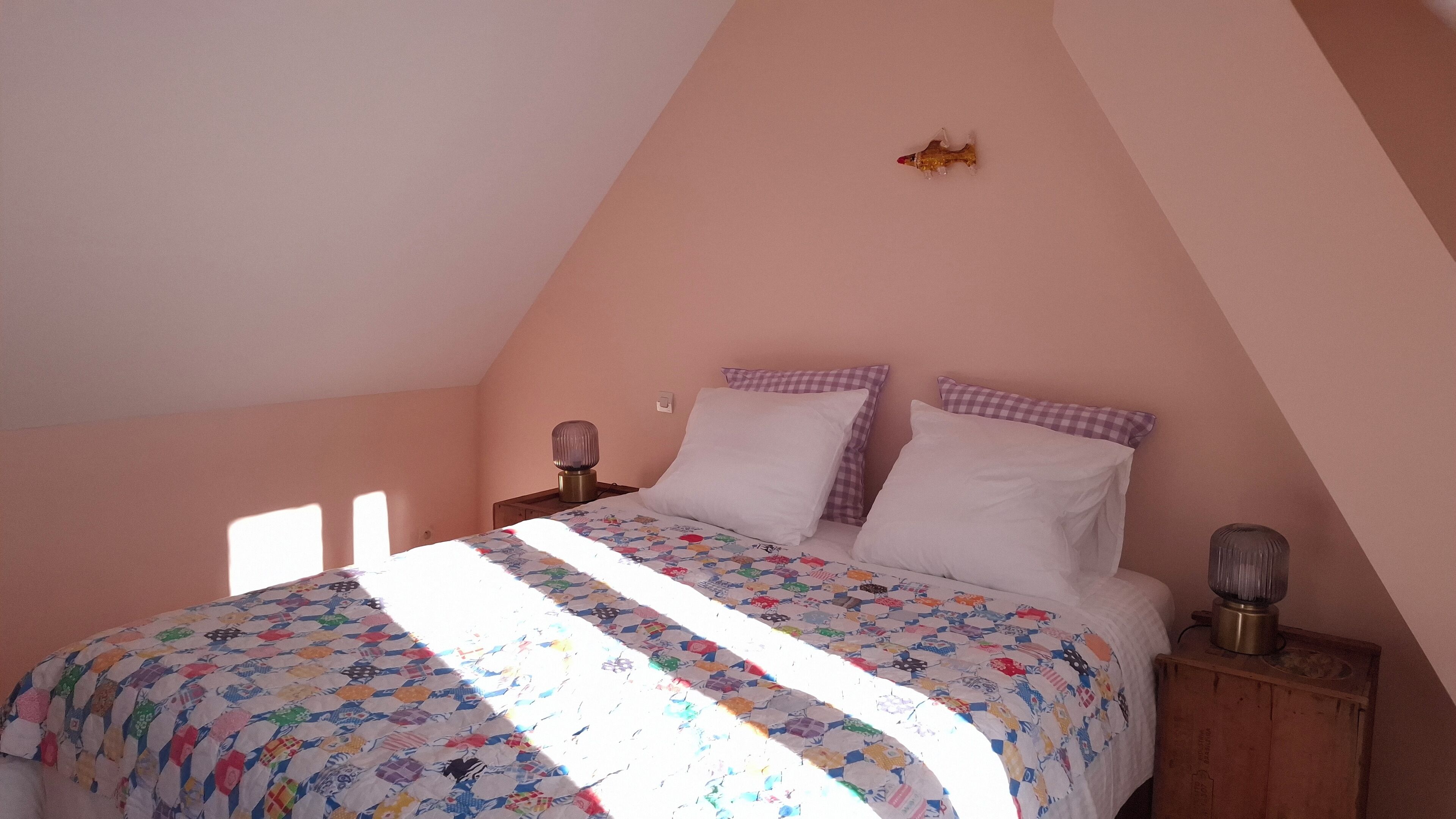 Una camera da letto con soffitto spiovente, un letto con copriletto colorato, due comodini con lampade e un piccolo oggetto decorativo a parete.