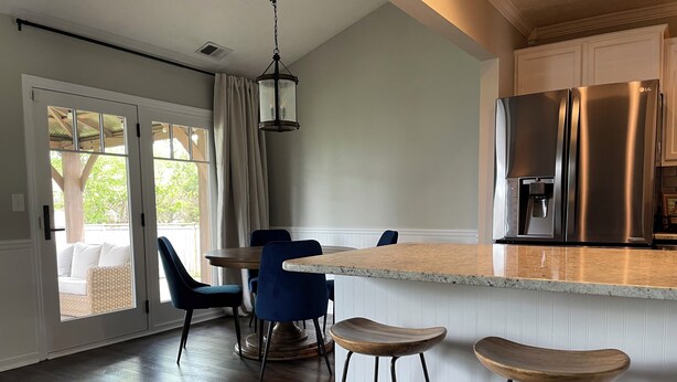 Une cuisine moderne avec un réfrigérateur en acier inoxydable, un îlot central en bois doté de tabourets, et un coin repas avec des chaises bleues.