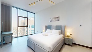 Een moderne hotelkamer met een groot bed, een bureau en uitzicht op de stads skyline door middel van kamerhoge ramen.