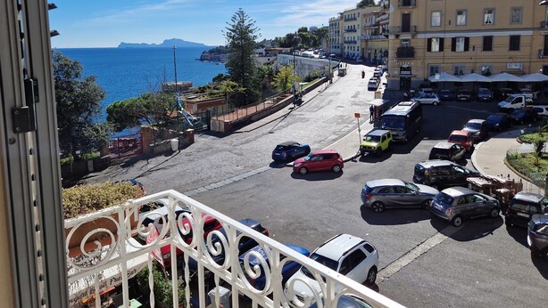 A coastal street with parked cars, a building with a sign 'ZIZZERIO', and a view of the sea. - Posillipo - panoramic apartment in the heart of the sea of Naples (Napoli)