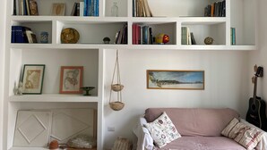 A living room with a striped sofa, a guitar, and a bookshelf filled with books. - Posillipo - panoramic apartment in the heart of the sea of Naples (Napoli)