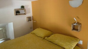 A bedroom with a bed, a bedside table, a wall-mounted shelf with a plant, and a wall-mounted light fixture. - Posillipo - panoramic apartment in the heart of the sea of Naples (Napoli)