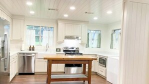 A modern kitchen with white cabinetry, a wooden table, and built-in appliances. - Lakefront fun for 14+pets w/game room deck sunsets (Whitney)